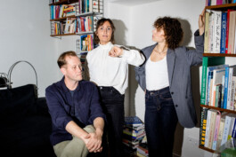 Drei Teammitglieder von neuerdings Dresden stehen vor einer Bücherwand und arbeiten gemeinsam, fotografiert von Judith Ziegenthaler. 